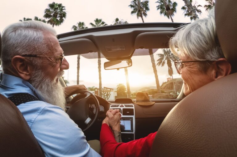 A happy older couple driving in a convertible car.
